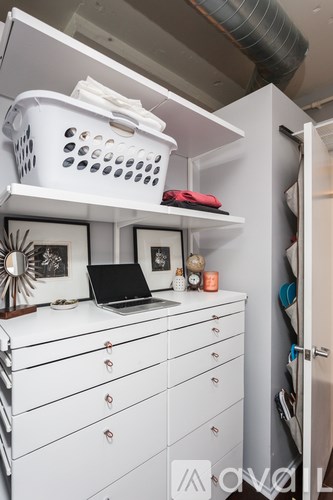 A white dresser with a laptop on top and a white basket on the shelf.