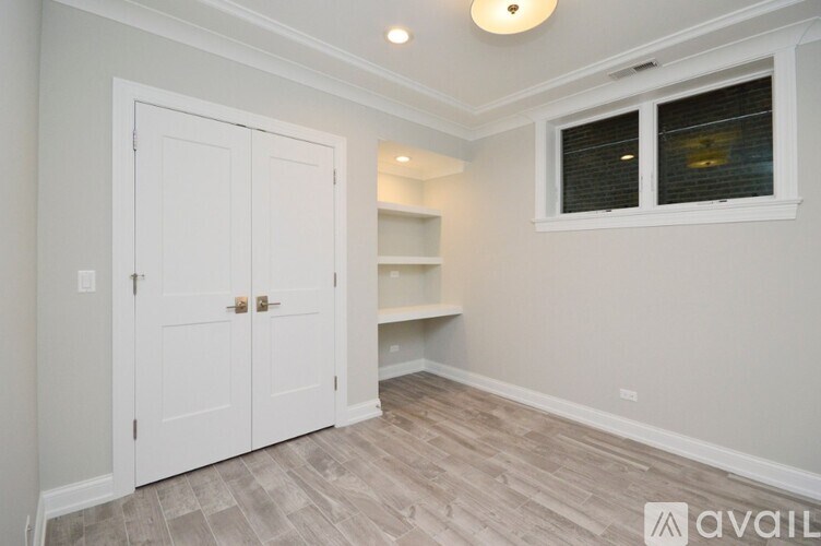 A room with a white door, a window with blinds, and a wooden floor.
