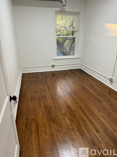 A room with wooden flooring and a window showing trees outside.