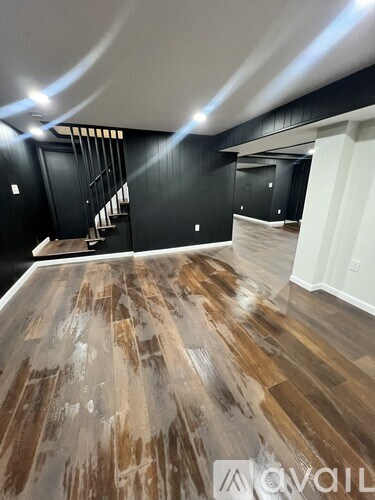 A room with wooden flooring and a staircase in the background.