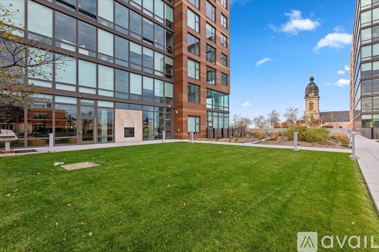 A grassy area in front of a modern building with a clock tower in the distance.