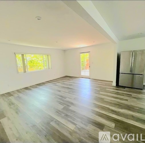 A spacious room with wooden flooring and a refrigerator in the corner.
