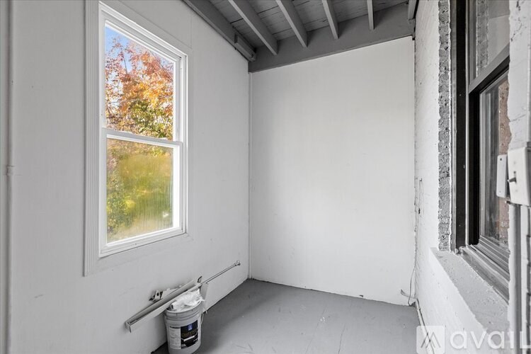A room with a window and a bucket of paint on the floor.