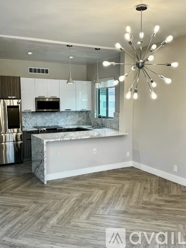 A modern kitchen with a marble island and a chandelier.