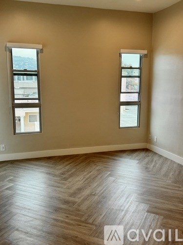A room with wooden flooring and two windows.