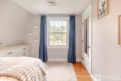 A bedroom with a bed, dressers, and a window with blue curtains.