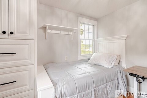 A white bedroom with a bed, dresser, and window.
