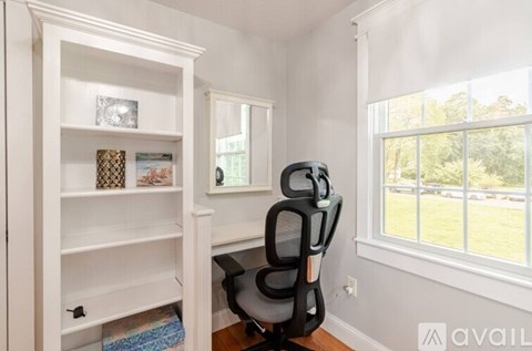 A white shelving unit with a mirror and a black chair in front of a window.