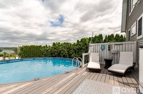A wooden deck with two chairs and a table is surrounded by a pool and trees.