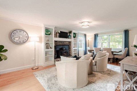 A living room with a white sofa, a white coffee table, a white floor lamp, a white clock, and a white fireplace.