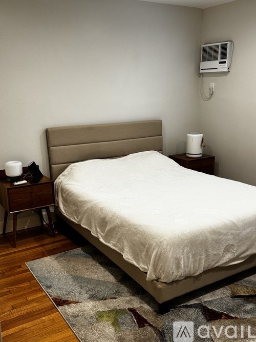 A bed with a white sheet and a brown headboard is in the image.