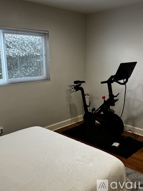 A black exercise bike is in a room with a white bed.