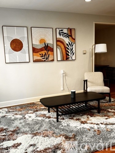A living room with a chair, a table, and three paintings on the wall.