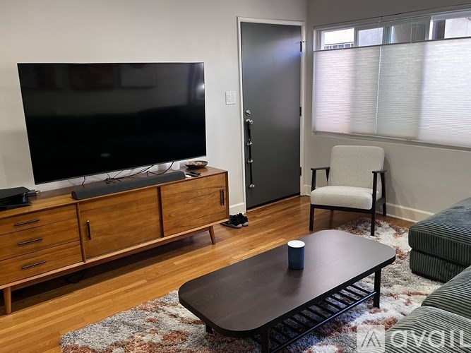 A living room with a flat screen TV, a wooden cabinet, a black coffee table, a chair, and a rug.