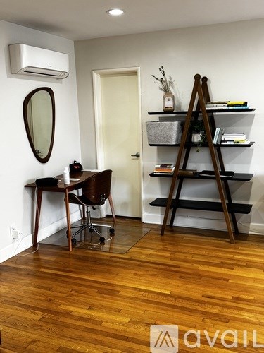 A room with a wooden floor, a desk with a chair, a mirror, and a shelf with a ladder.