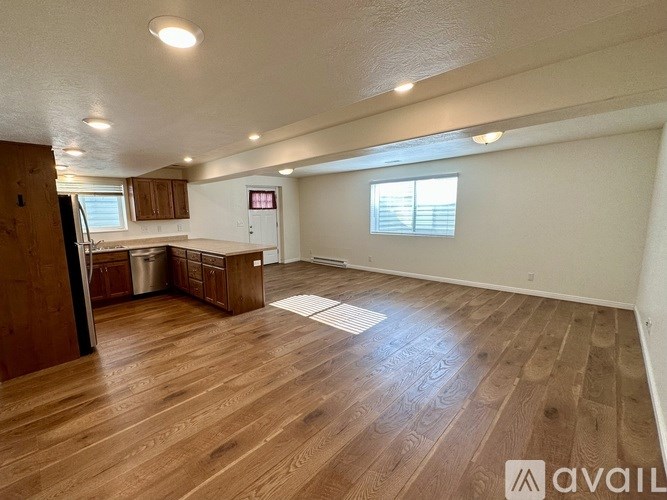 A spacious room with wooden flooring and a kitchen area in the background.