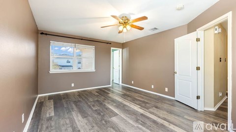 A room with a ceiling fan and a window showing a view of a building.