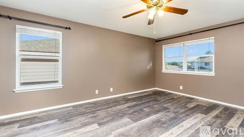 A room with a ceiling fan and two windows.
