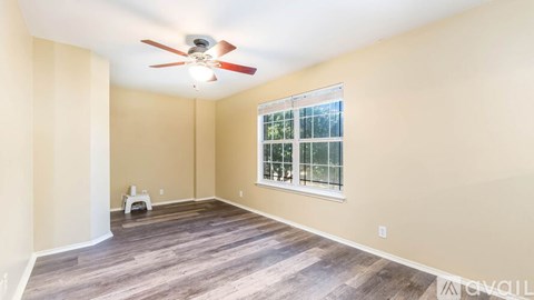 A room with a ceiling fan and a window with a view of trees.
