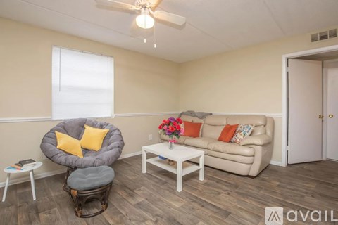A living room with a grey chair, a white sofa, and a small table with a vase of flowers on it.