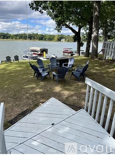 A white table and chairs are set up on a lawn with a lake and boats in the background.