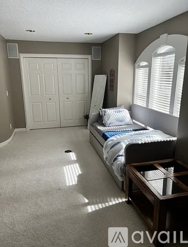 A bedroom with a bed, nightstand, and a window with blinds.