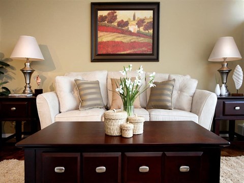 A living room with a white couch, a painting on the wall, and a wooden table with baskets on it.