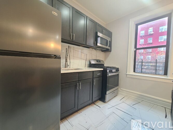 A kitchen with a stainless steel refrigerator, black cabinets, and a window overlooking a red building.