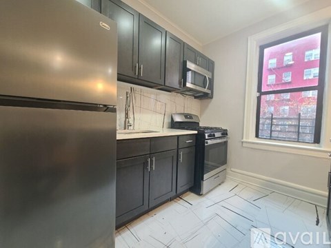 A kitchen with a stainless steel refrigerator, black cabinets, and a window overlooking a red building.