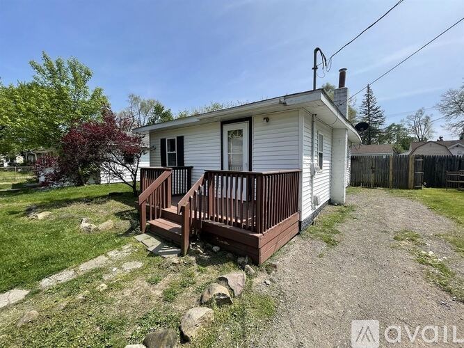 A small white house with a brown deck in the front yard.