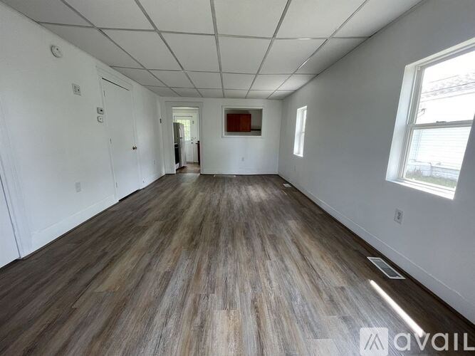 A spacious room with wooden flooring and white walls.