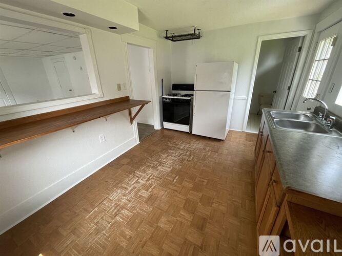 A kitchen with a white refrigerator, wooden flooring, and a stainless steel sink.