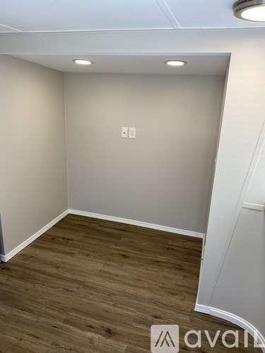 A room with wooden flooring and a white wall with a switch.
