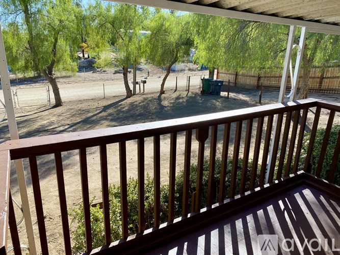 A balcony with a view of a dirt field and trees.