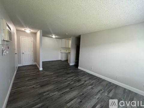 A room with wooden flooring and white walls, with a door on the left and a cabinet on the right.
