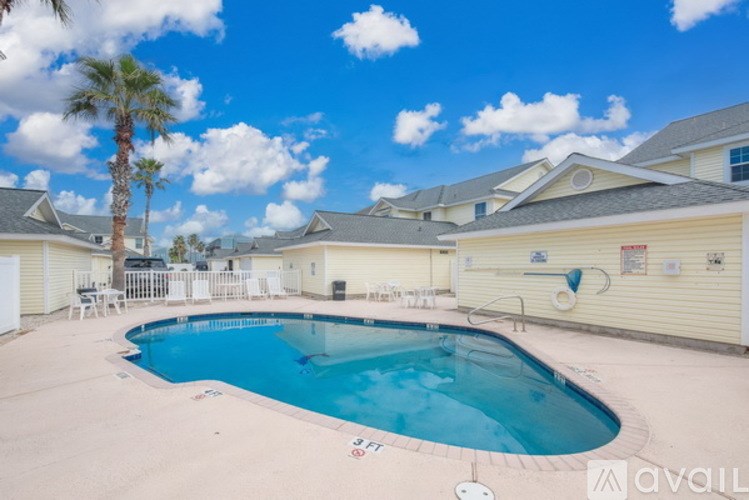A swimming pool surrounded by a sandy area and a few chairs.