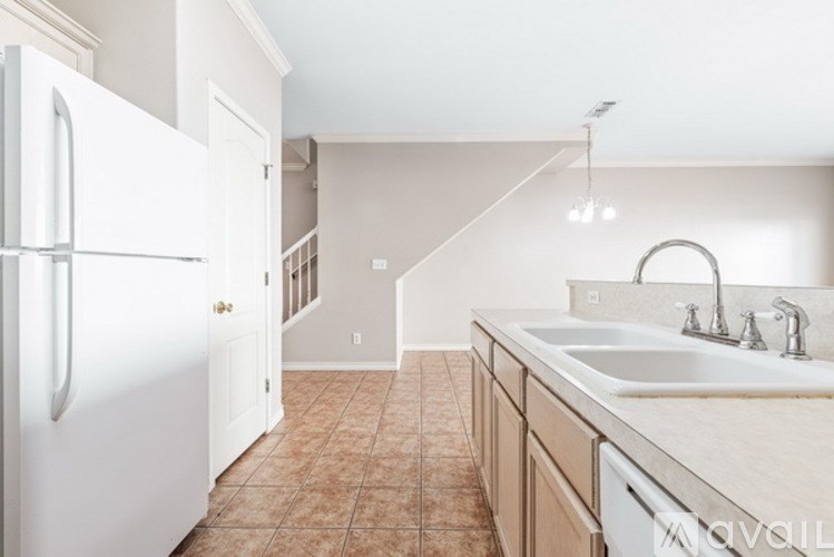A kitchen with a white fridge, brown tiles and a white sink.
