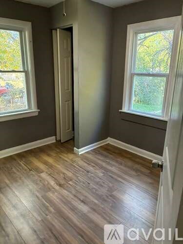 A room with wooden flooring and two windows.