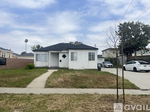 A white house with a black roof is situated in a residential area with a car parked in the driveway.