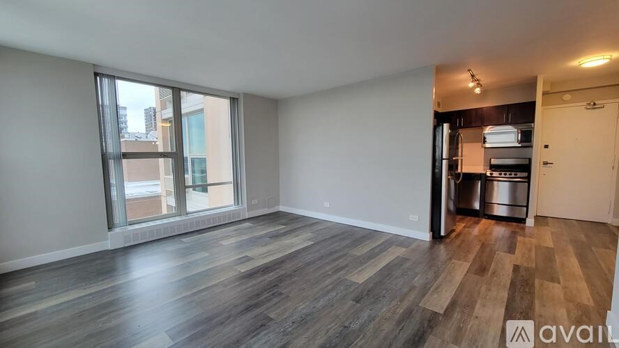 A room with wooden flooring and a kitchenette in the back.
