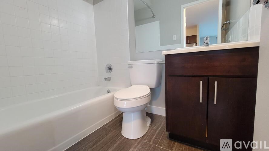 A white toilet sits in a bathroom with a wooden cabinet and a white bathtub.