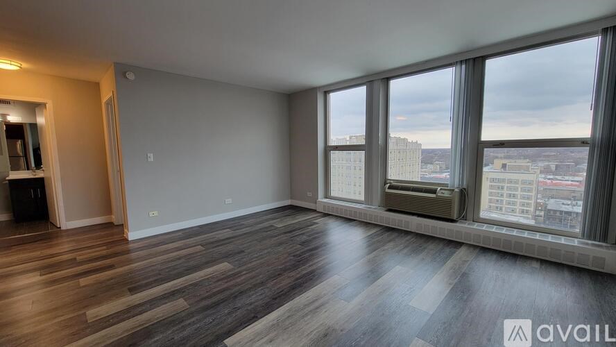 A spacious room with wooden flooring and large windows overlooking a cityscape.