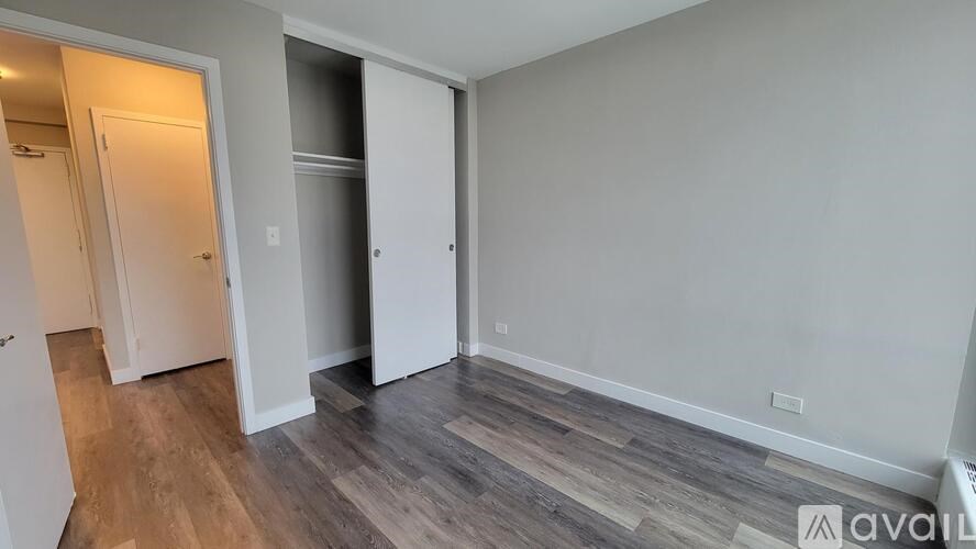 A room with a wooden floor and white walls, with a doorway leading to another room.