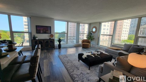 A living room with a couch, a chair, a coffee table, and a large window overlooking a cityscape.