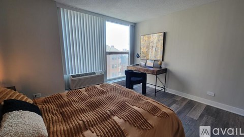 A bedroom with a bed, a desk, and a window with blinds.