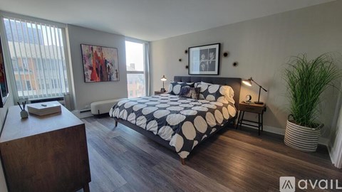 A bedroom with a bed, nightstand, and a plant.