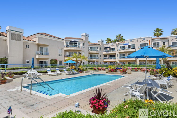A large pool surrounded by chairs and umbrellas in front of apartment buildings.