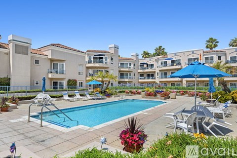 A large pool surrounded by chairs and umbrellas in front of apartment buildings.