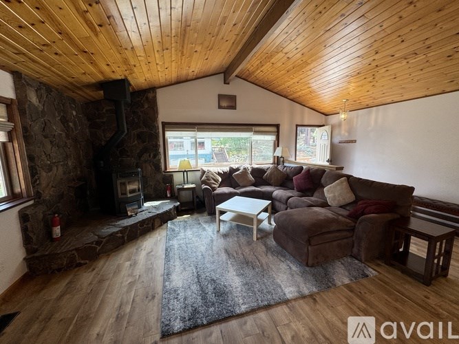 A living room with a stone fireplace and wooden ceiling.