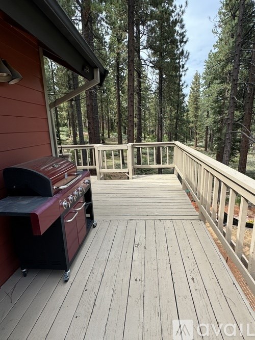 A red grill is on a wooden deck with a railing.